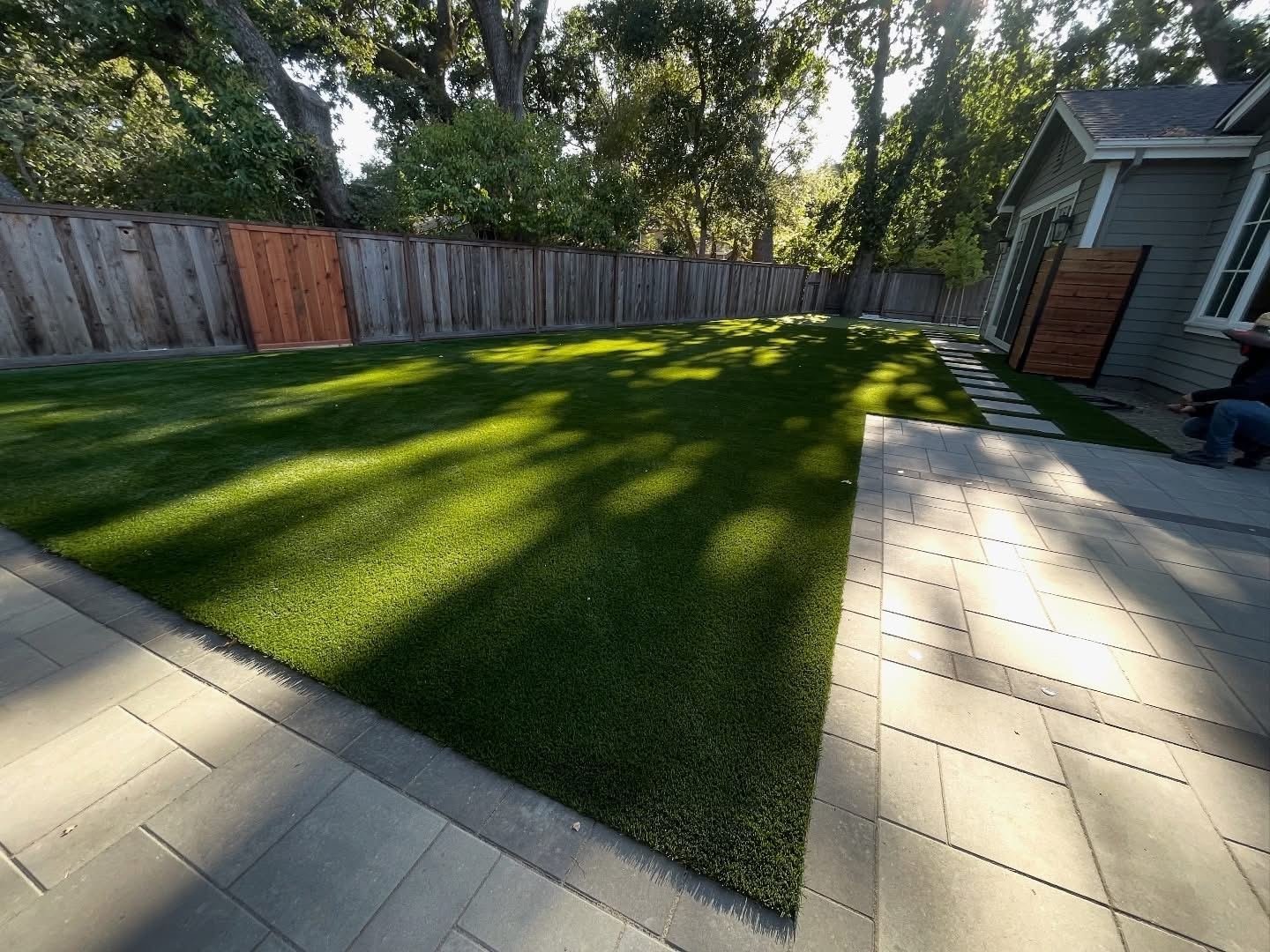 Manicured artificial turf backyard with paver patio and modern siding